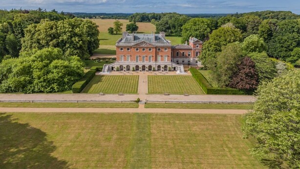 Een groot, historisch gebouw met een symmetrische gevel, omgeven door keurig onderhouden gazons en bomen.
