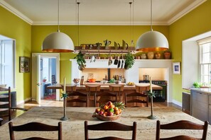 Un coin repas avec une table et des chaises en bois, un panier de fruits et des ustensiles de cuisine suspendus.