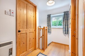 Un couloir avec des portes en bois, une fenêtre ornée de rideaux à motifs et un radiateur fixé au mur.