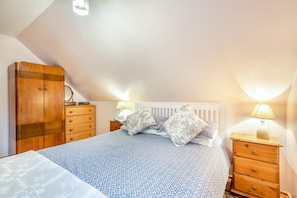 Une chambre à coucher comprenant un lit, deux tables de chevet, une armoire et un plafond en pente.