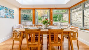 Uma sala de jantar com pé-direito alto, janelas amplas e vista para o jardim.