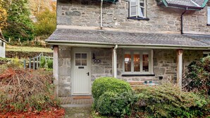 A stone house with a white door, a small porch, and a window. - 2 Bed in Maentwrog (oc-g28262) (Maentwrog)