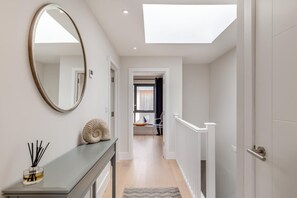 A hallway with a skylight, a round mirror, a console table with a decorative shell, and a view into a room with a sailboat model. - 2 Bed in Harlyn Bay (oc-a28321) (Harlyn Bay)