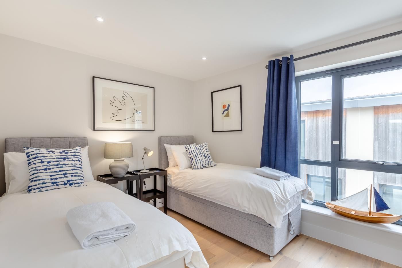 Een hotelkamer met twee bedden, een raam met gordijnen en kunstwerken aan de wanden.