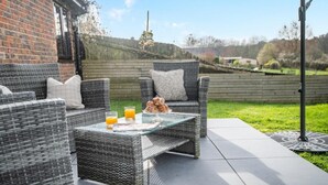 A patio with wicker furniture, a glass table, and a view of a brick building and hills. - 2 Bed in Chalbury (oc-t28279) (Horton)