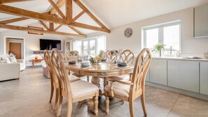 A spacious dining area with a wooden table and chairs, a kitchen in the background, and a large window providing natural light. - 2 Bed in Chalbury (oc-t28279) (Horton)