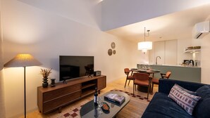Un salon moderne doté d’un téléviseur à écran plat, d’un canapé, d’une table basse avec un livre, et d’un coin repas avec des chaises et une table.