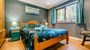 Ein Schlafzimmer mit einem hölzernen Bett, einem Nachttisch, einer Lampe, einem Fenster mit Vorhängen und einem Gemälde an der Wand.