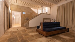 Une pièce spacieuse dotée d’un sol en pierre, d’un escalier en bois, d’un canapé bleu et d’un bureau en bois avec une lampe.