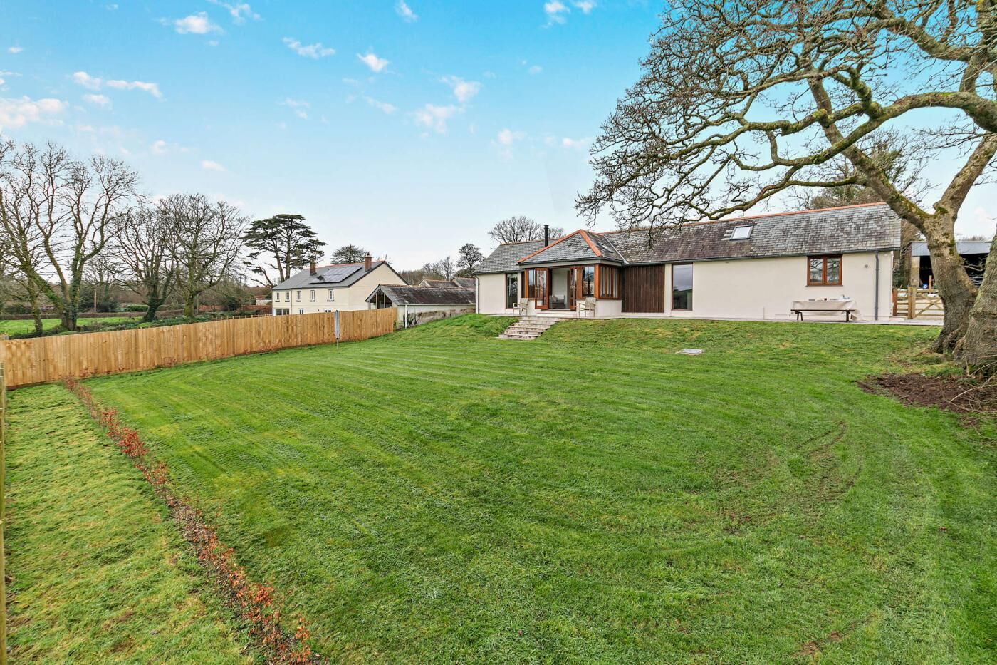 A residential property with a well-maintained lawn, a wooden fence, and a house with a sloped roof.