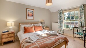Une chambre à coucher avec un lit, des tables de chevet, une lampe, un radiateur, une fenêtre avec des rideaux et un tableau au mur.