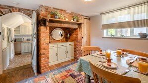 Une cuisine chaleureuse avec un mur en briques, des armoires en bois et un coin repas où une table est dressée pour le petit-déjeuner.