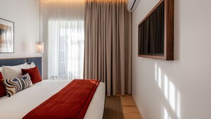 Una habitación de hotel con cama, ventana con cortinas, unidad de aire acondicionado instalada en la pared y un cuadro enmarcado.