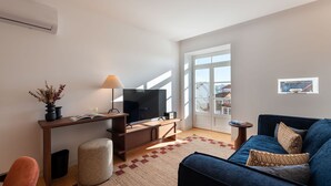 Una sala moderna con televisor, escritorio, sofá y ventana con vistas a edificios.