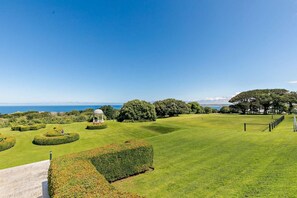 Ein gepflegter Rasen mit einem Gartenpavillon, ordentlich geschnittenen Hecken und Blick auf das Meer.