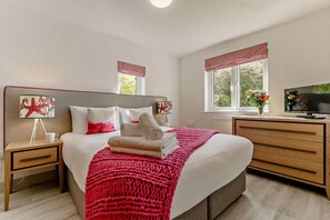 Une chambre à coucher avec un lit, des tables de chevet, une télévision et des fenêtres avec des rideaux.