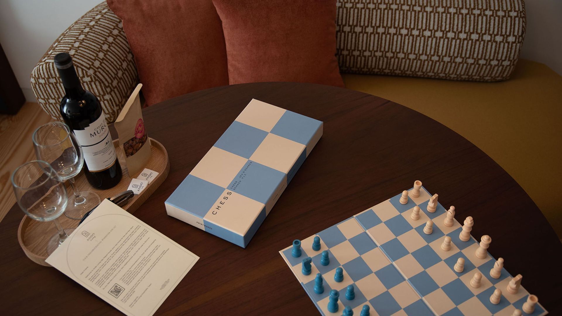 A chessboard, a bottle of wine, glasses, and a box on a round table.