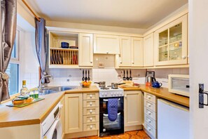Een kleine keuken met een spoelbak, fornuis, oven en keukenkastjes.