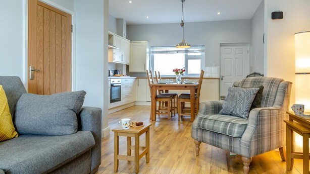 A modern living room with a grey sofa, a plaid armchair, and a wooden coffee table. A dining area with a wooden table and chairs is visible in the background. - 2 Bed in Amble (oc-b28345) (Amble)