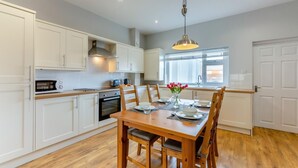 A modern kitchen with white cabinetry, a wooden dining table, and a hanging pendant light. - 2 Bed in Amble (oc-b28345) (Amble)