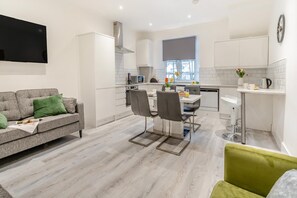 A modern kitchen with white cabinets, a dining area with a table and chairs, and a grey sofa with green cushions. - 3 Bed in Cardiff (oc-h28347) (Cardiff)