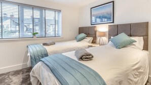 Quarto de hotel com duas camas, uma janela com persianas, abajur e um quadro na parede.