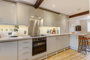 Cozinha moderna com eletrodomésticos de aço inoxidável, armários brancos e piso de madeira.