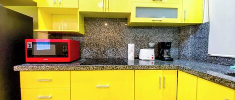 Une cuisine avec des meubles de couleur jaune, un four à micro-ondes rouge, un grille-pain et une machine à café, le tout posé sur un plan de travail en granit.