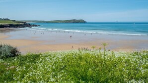 Ein Strand mit Menschen, Grünflächen und Hügeln im Hintergrund.