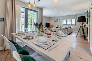 A modern dining area with a long table set for a meal, a sofa in the background, and a tripod lamp.