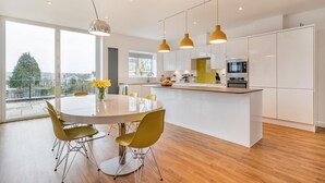 A modern kitchen with white cabinets, a central island, and yellow pendant lights. - 4 Bed in Killay (oc-c28372) (Killay)