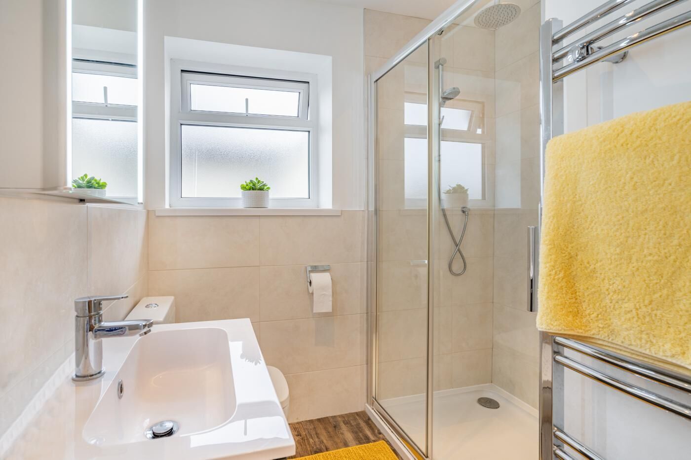 A modern bathroom with a glass shower enclosure, a white sink, and a yellow bath mat.
