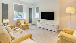 A modern living room with a sofa, armchair, and a flat-screen TV mounted on the wall. - 4 Bed in Killay (oc-c28372) (Killay)