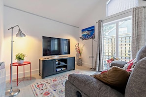 Un salon moderne avec un téléviseur à écran plat, une petite table d’appoint rouge ornée d’une plante, un lampadaire et un canapé.