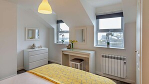 Ein Schlafzimmer mit Bett, Kommode, Schminktisch und zwei Fenstern mit Blick.