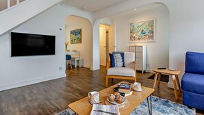 Ein modernes Wohnzimmer mit Flachbildfernseher, Essbereich mit Tisch und Stühlen, einem blauen Sofa und einer Treppe.