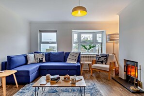 Ein modernes Wohnzimmer mit einem blauen Sofa, einem Couchtisch, einem Kamin und Blick durch große Fenster.