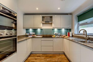 A compact kitchen with built-in appliances, a window, and a wooden floor. - 3 Bed in Porthleven (oc-s28377) (Porthleven)