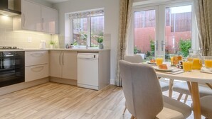 Une cuisine moderne avec des meubles blancs, un lave-vaisselle et un coin repas où la table est mise pour le petit-déjeuner.