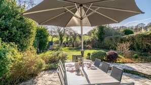 Un espace extérieur aménagé pour les repas, avec une table et des chaises, un grand parasol et un chemin en pierre.