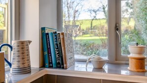 Un comptoir de cuisine avec vue sur la fenêtre, une bouilloire, un pichet, un bol et une rangée de livres.