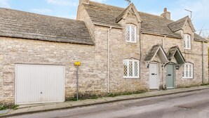 Il s’agit d’un bâtiment traditionnel en pierre, doté d’un grand portail de garage, d’une petite entrée avec une porte verte et d’une cheminée.