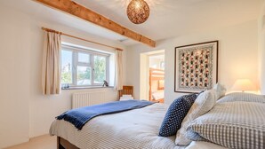 Une chambre avec un grand lit, une fenêtre avec des rideaux, une poutre en bois au plafond et une lampe fixée au mur.