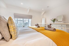 A hotel room with a large bed, a bedside table with a mirror, and a view of the outdoors through a window.