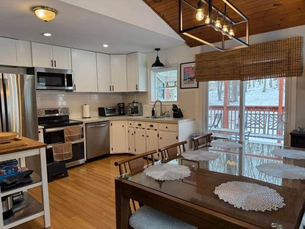 A modern kitchen with white cabinets, stainless steel appliances, and a wooden dining table with lace placemats.