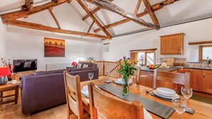 Un vaste espace de vie doté d’un plafond en bois, d’un canapé, d’une table à manger pour deux personnes et d’une cuisine située à l’arrière-plan.