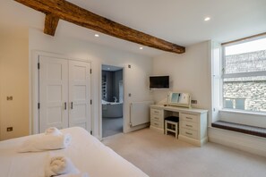 A bedroom with a bed, a desk, a TV, and a window with a view of a stone wall.