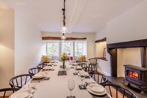 A dining room with a long table set for a meal, a fireplace, and large windows.