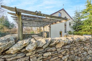 En stenmur, en träpergola och ett modernt hus med ett sluttande tak.
