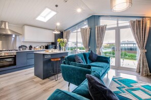 Une cuisine moderne avec un îlot central, un canapé de couleur turquoise et une vue sur l’extérieur grâce à de grandes fenêtres.